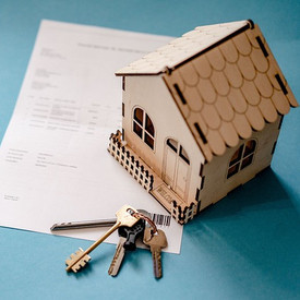 Modell eines Hauses mit Haustürschlüsseln und einem Kaufvertrag